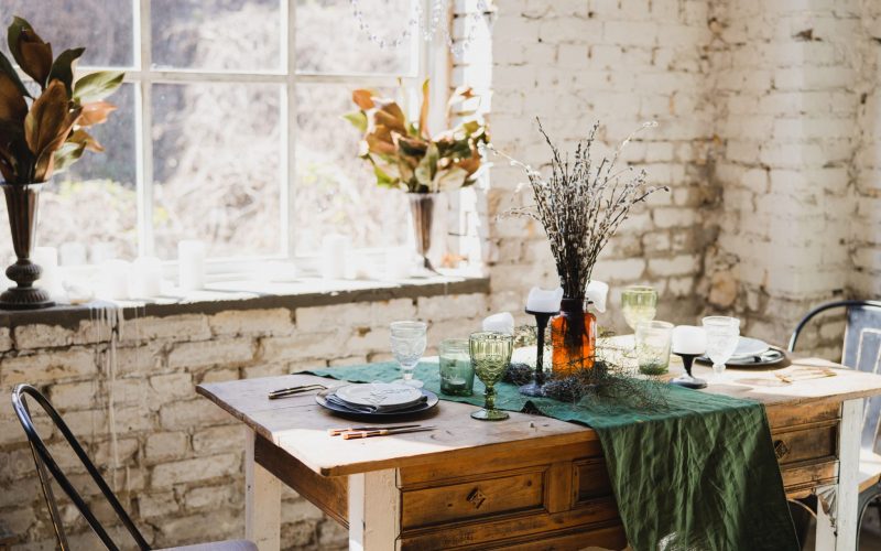 Coziness at home. Modern interior design. Beautiful vintage dining table with decorations, flowers, candles and laying near the window. Loft, botanic, rustic style. Table set for an event, party, date or wedding.